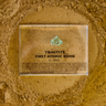 Close-up of a fragment of Trinitite, a material formed from the first atomic bomb explosion, embedded in clear acrylic. The piece has a greenish tint and a rough, uneven surface with visible texture, reflecting its unique origin from the historic Trinity test.